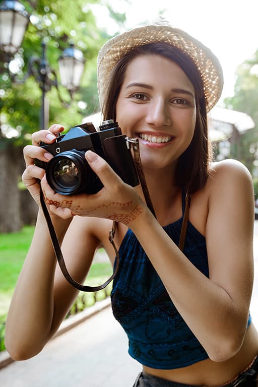 jeune femme souriante avec un chapeau prenant des photos