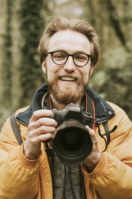 photographe homme souriant tenant appareil photo dans les bois