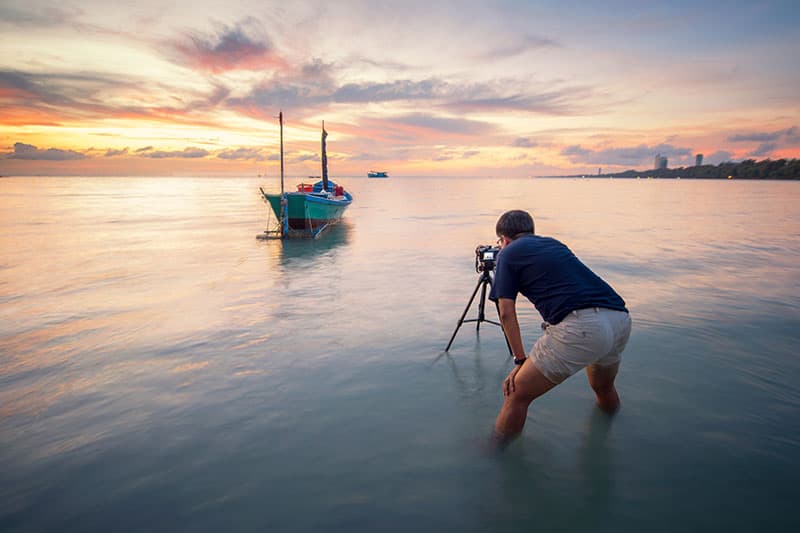 photographe qui prend une photo du lever du soleil avec un bateaux de peche