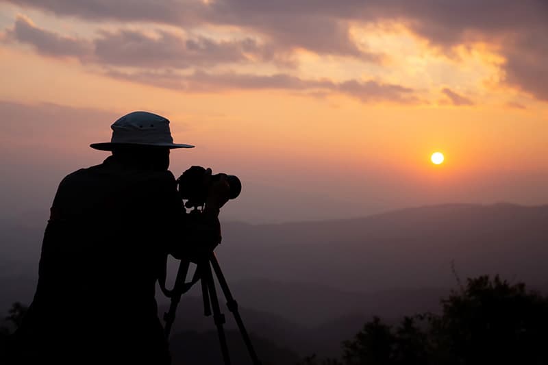 silhouette d'un photographe qui photographie un coucher de soleil dans les montagnes